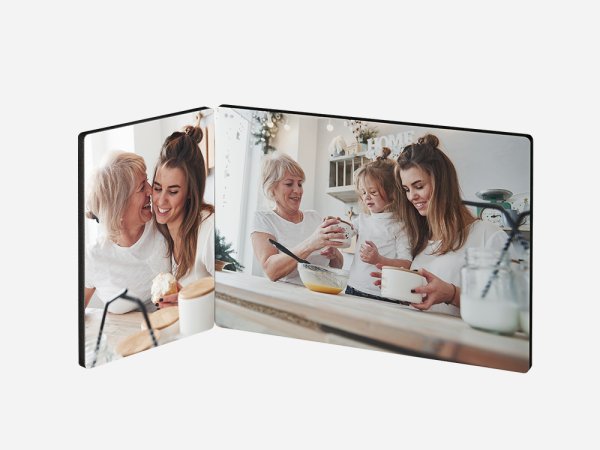 Ein zweiteiliger Fotoaufsteller zeigt zwei fröhliche Szenen in einer Küche. Auf der linken Seite umarmen sich eine ältere Frau mit weißen Haaren und eine junge Frau mit braunen Haaren und lachen. Sie stehen an einem Tisch mit einer Glasflasche.